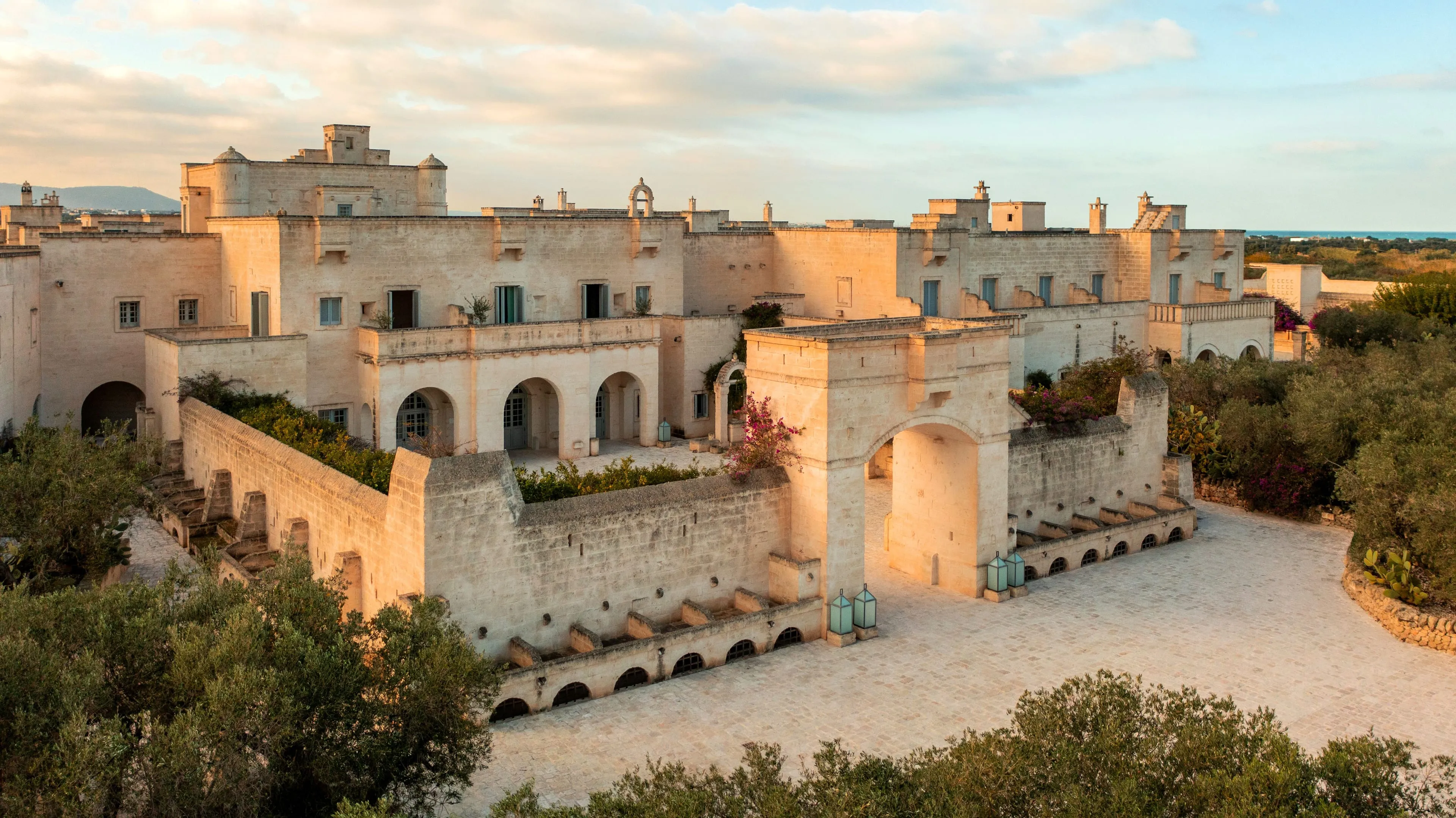 The arched gateway into the Borgo Egnazia wedding venue at sunset, tufo walls above the drive with the Adriatic beyond the olive groves