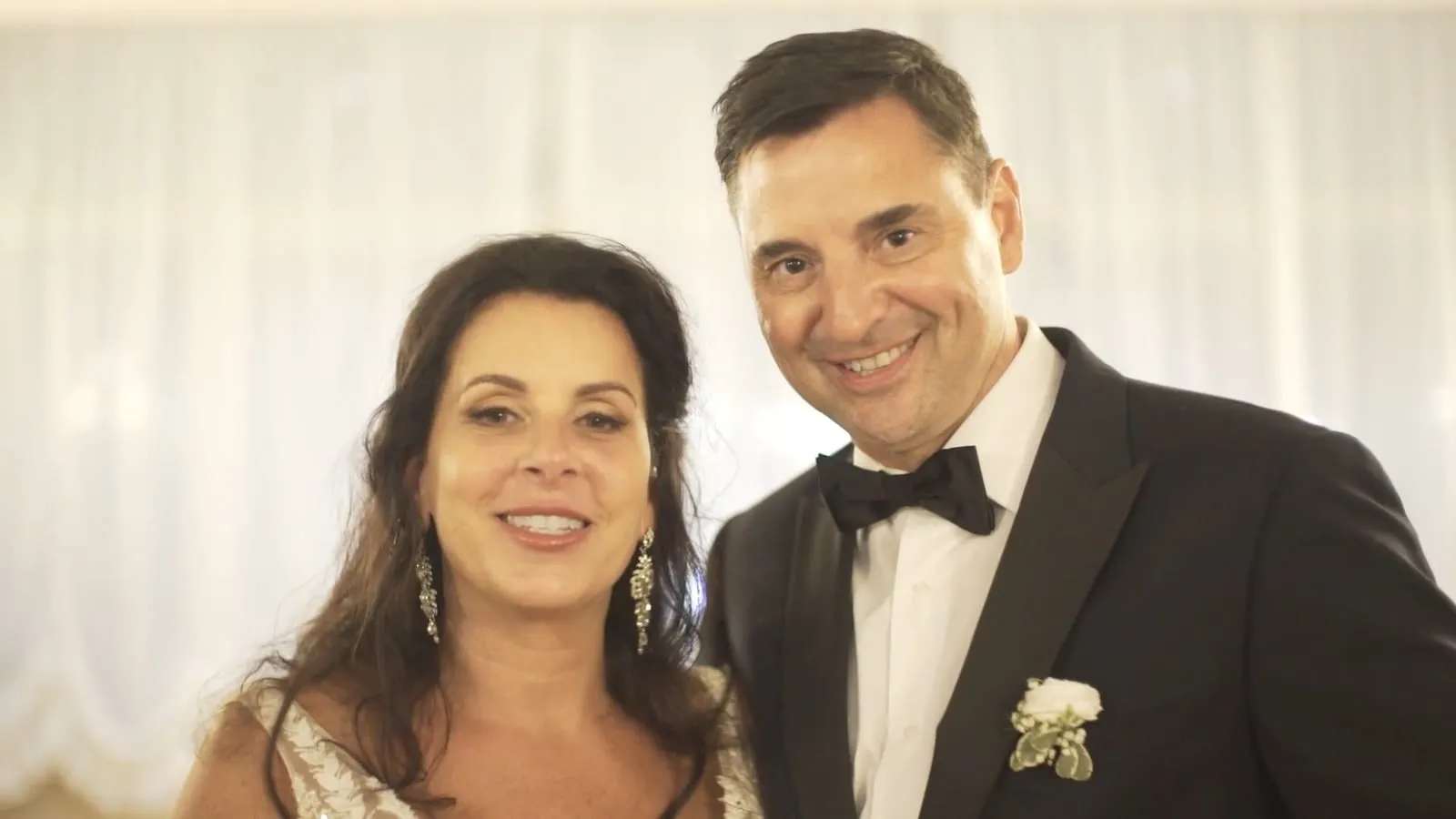 Deb and Steven in front of white curtains, talking about their wedding